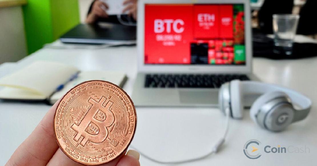 Bitcoin érme egy női kézben és a bitcoin árfolyam mozgásai a coin360 weboldalon háttérben.