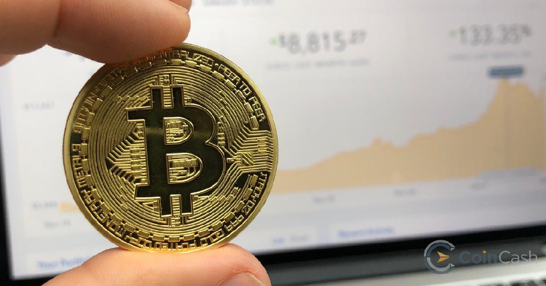 Bitcoin érme egy férfi kézben, háttérben a bitcoin árfolyammal.